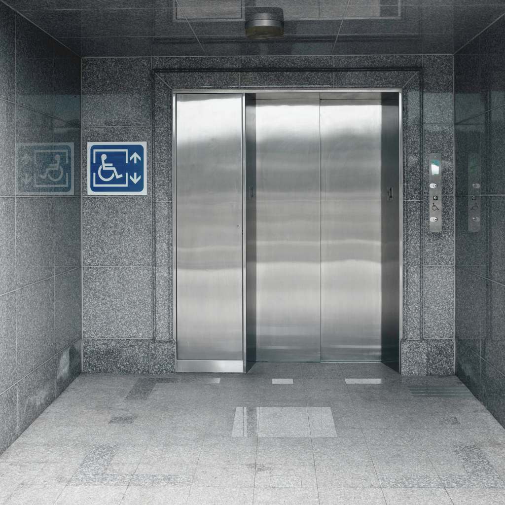 Stainless steel elevator with clear wheelchair accessibility signage and compliant call buttons, showing a California building entrance that meets ADA and Title 24 access requirements.