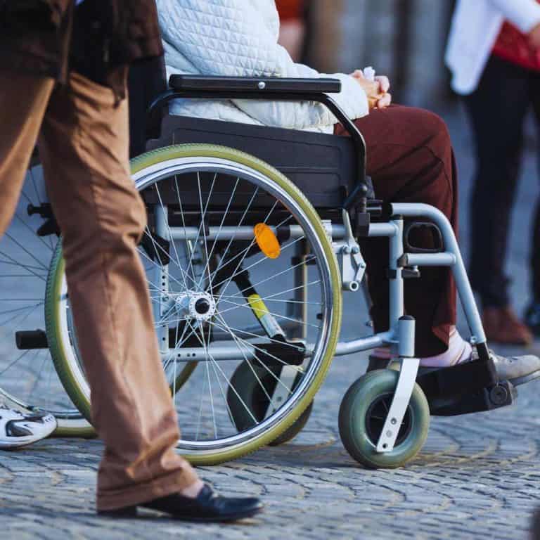 A person in a wheelchair moving along a city sidewalk with uneven pavement, highlighting real-world ADA accessibility challenges in California.