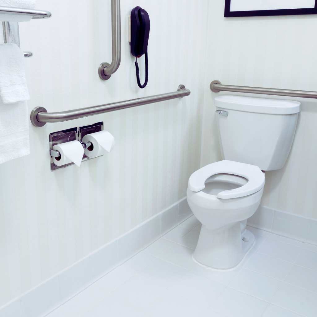 Toilet area in an accessible California restroom showing side and rear grab bars, correct mounting heights, and clear wall space used to illustrate ADA and Title 24 toilet dimension requirements.