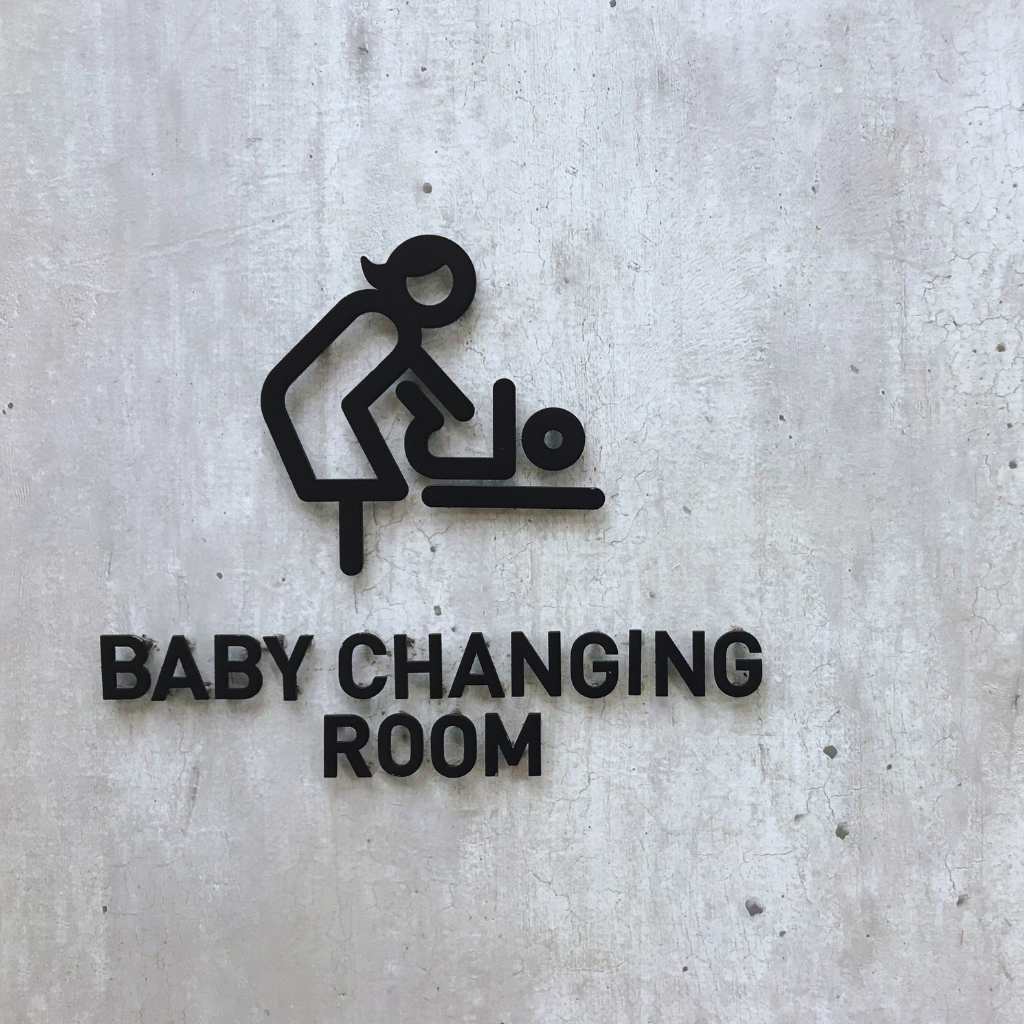 Black baby changing room wall sign showing a caregiver using a changing table in a public restroom setting.