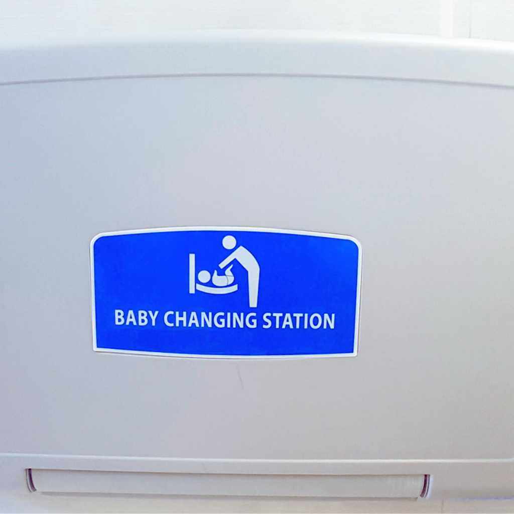 a blue ADA-compliant baby changing station sign on a wall-mounted changing table in a public restroom.