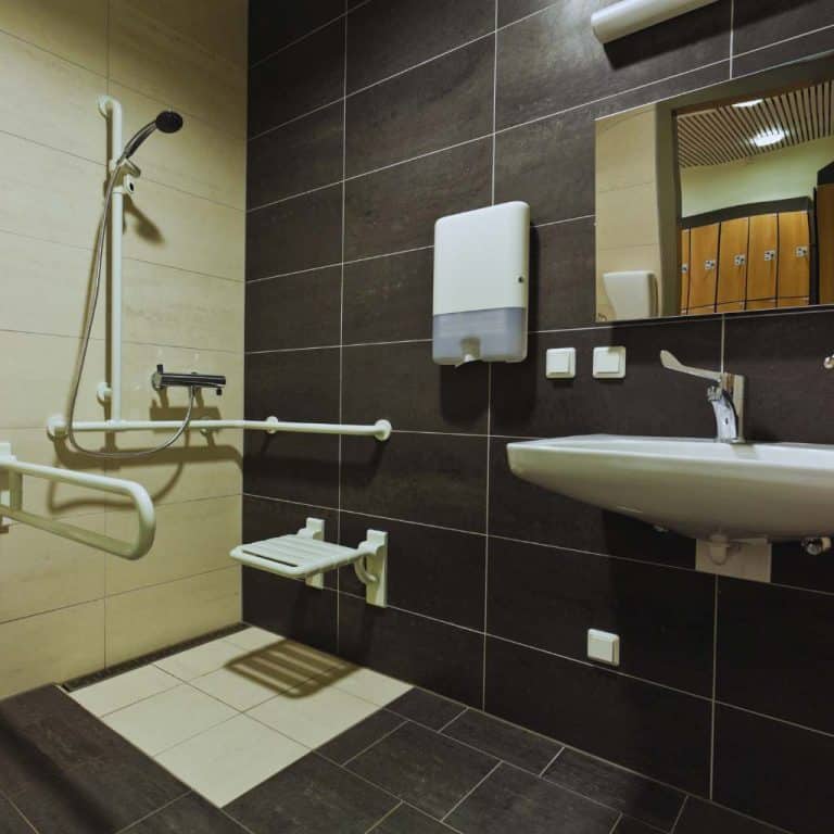 Accessible California bathroom showing compliant grab bars, fold-down shower seat, reachable fixtures, and required sink clearances used to demonstrate ADA and Title 24 dimensional standards.