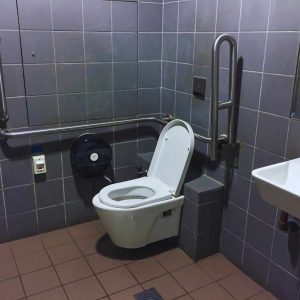 Accessible restroom in California showing a wall-mounted toilet with side and rear grab bars, correct clearances, and fixture placement that aligns with ADA and Title 24 bathroom dimension requirements.