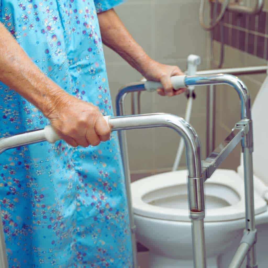Older adult holding a walker beside a toilet, illustrating the need for adequate ADA and Title 24 clear floor space for safe transfers in accessible bathrooms.