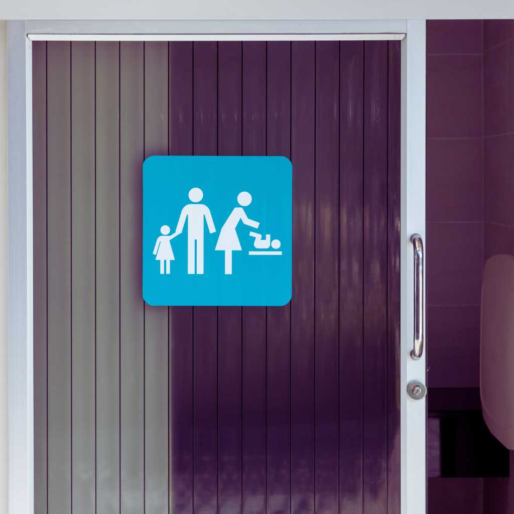 Blue square sign with white icons of two adults, a child, and a baby on a changing table displayed on a black-panelled restroom door