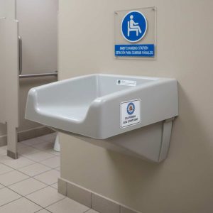 A wall-mounted baby changing station labeled "California ADA Compliant," installed in a tiled public restroom with accessibility signage above.