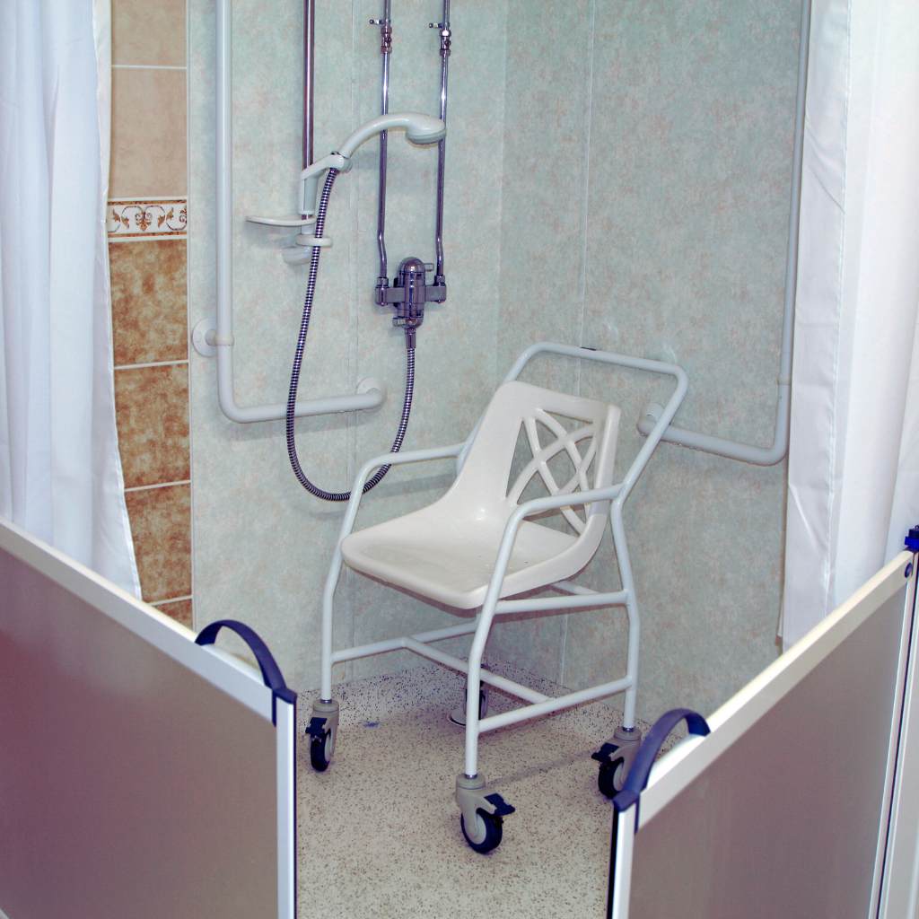 Accessible roll-in shower with a shower seat, horizontal and vertical grab bars, and handheld shower spray mounted on the wall